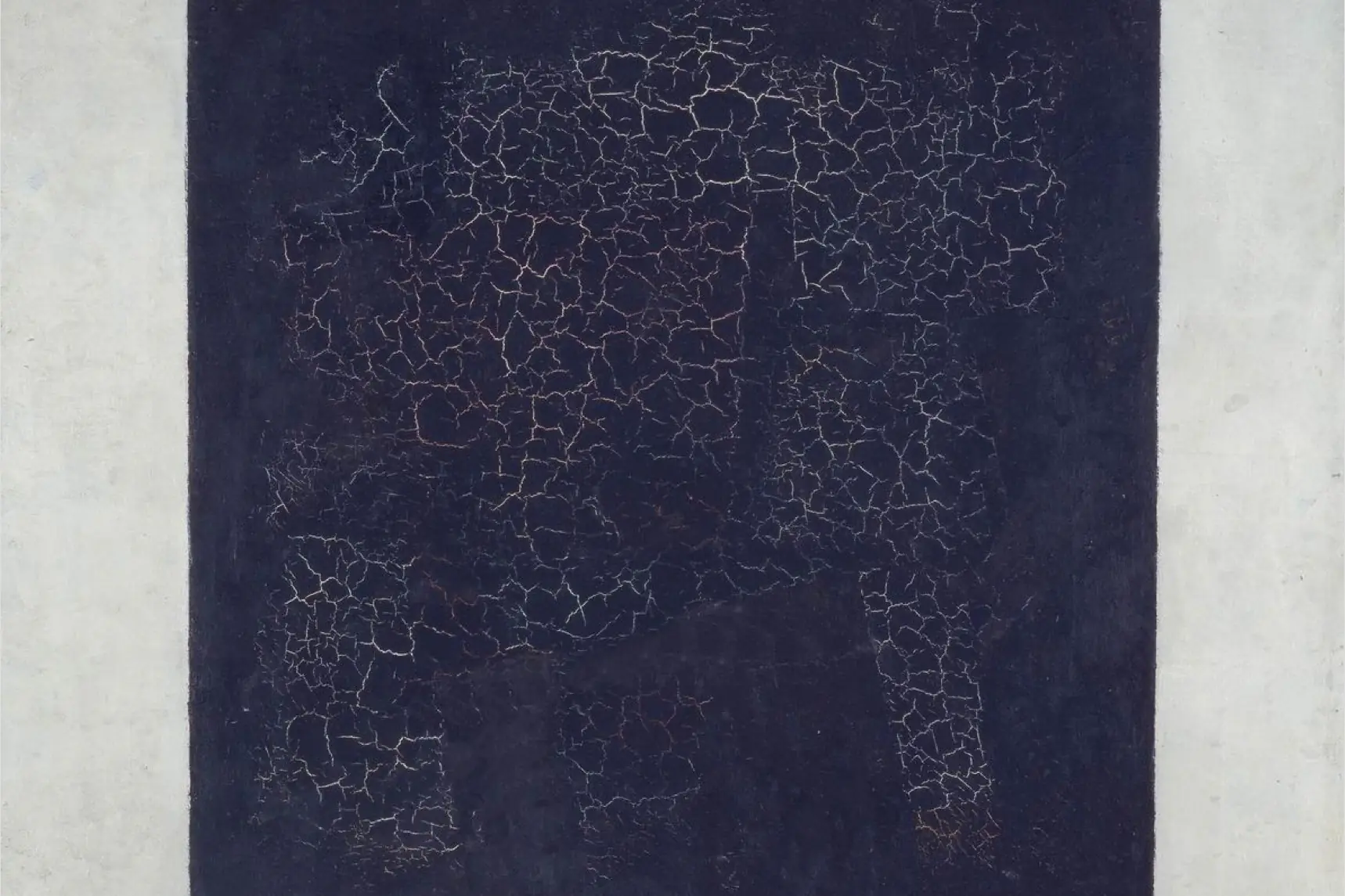 A detail of Kazimir Malevich's Black Square: a field of cracked black paint between two bands of white canvas